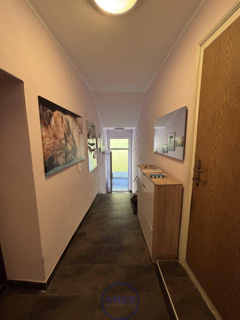 Langer Flur mit dunklen Fliesen, rosa Wänden und einem Eingangsbereich.