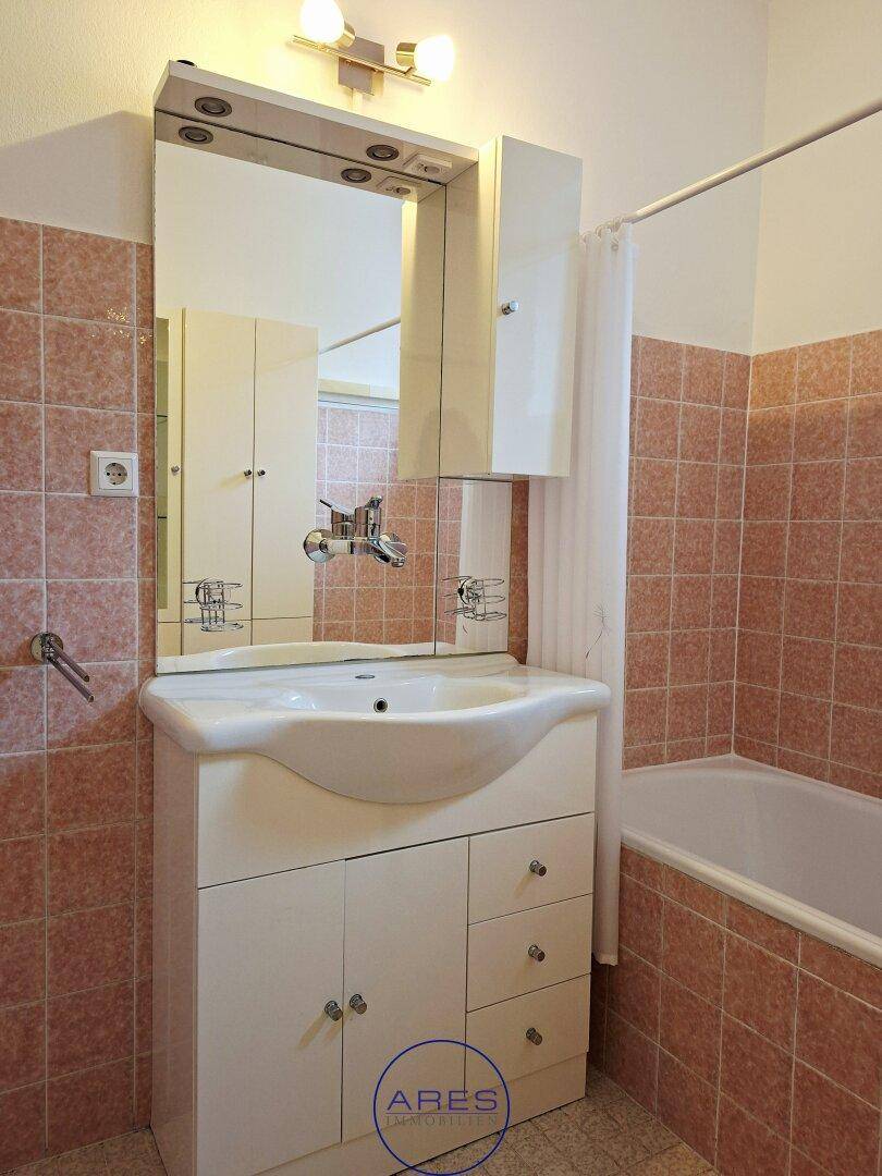 Badezimmer im 80er-Jahre-Stil mit rosa Fliesen, Badewanne und Waschtisch mit Spiegelschrank.
