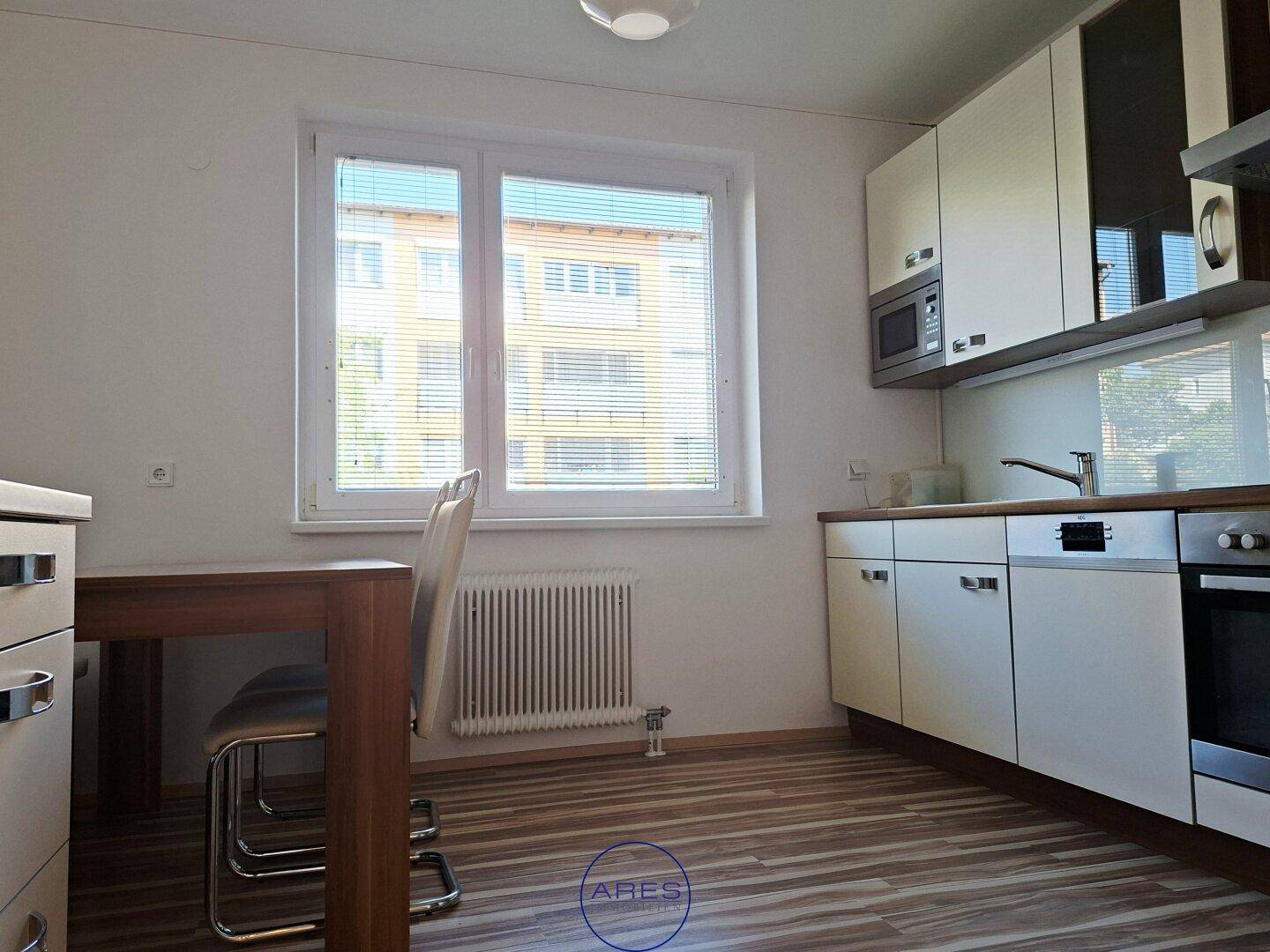 Küchenbereich mit Fenster, Esstisch und Laminatboden, bietet Platz für Mahlzeiten.