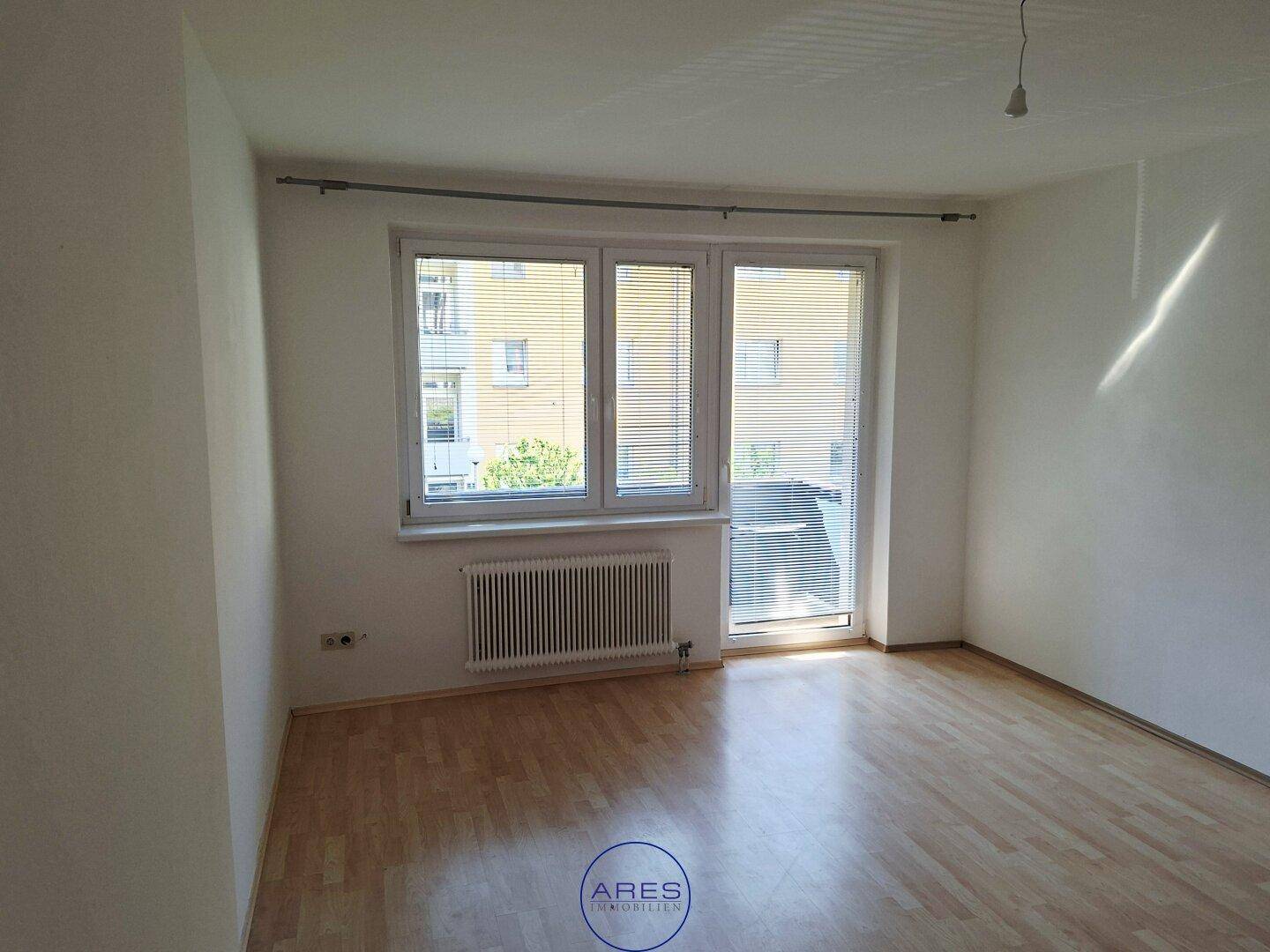 Leeres Wohnzimmer mit Laminatboden und Zugang zu einem Balkon, hell und geräumig.