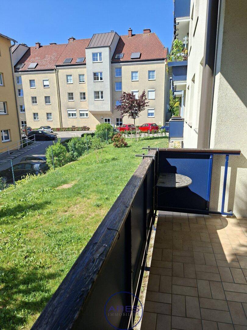 Kleiner Balkon mit Fliesenboden und Blick auf die grüne Umgebung und Nachbargebäude.
