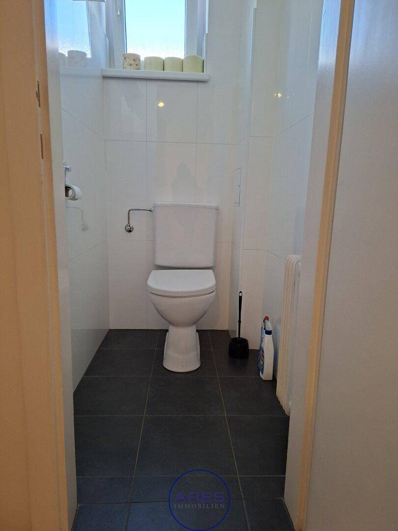 Separates WC mit dunklen Bodenfliesen und weißer Wandverkleidung, funktional und sauber.