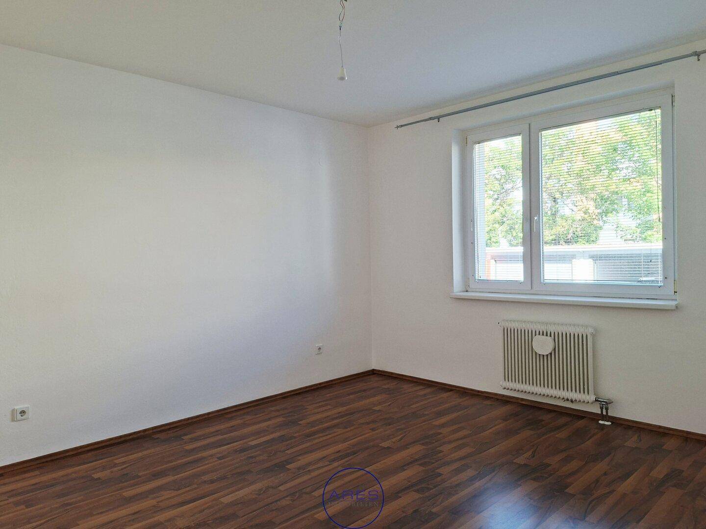 Helles Schlafzimmer mit dunklem Laminatboden und großem Fenster, bietet viel Tageslicht.