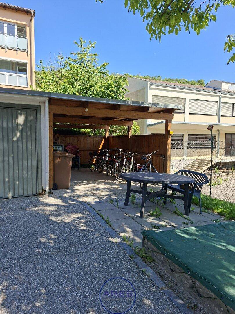Überdachter Fahrradabstellplatz und Außenbereich mit Sitzgelegenheiten neben dem Gebäude.
