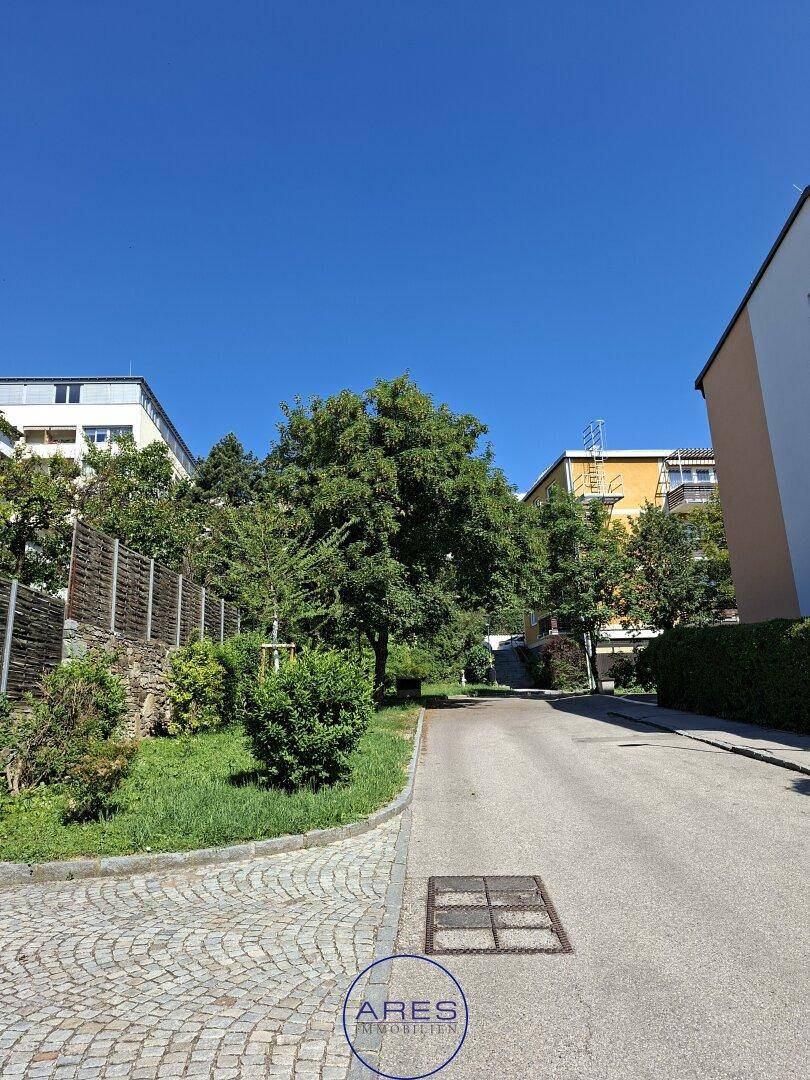 Ruhige Wohnstraße mit Bäumen und gepflastertem Bereich, umgeben von Gebäuden.