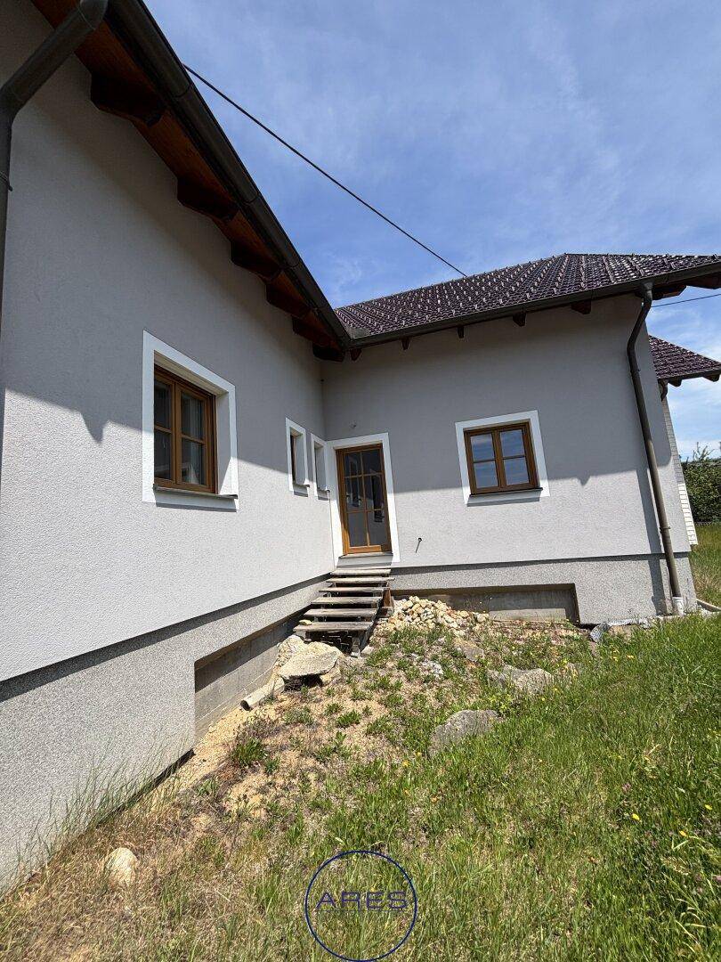 Seitenansicht des Hauses mit Eingangsbereich und einfacher Steintreppe im Grünen.