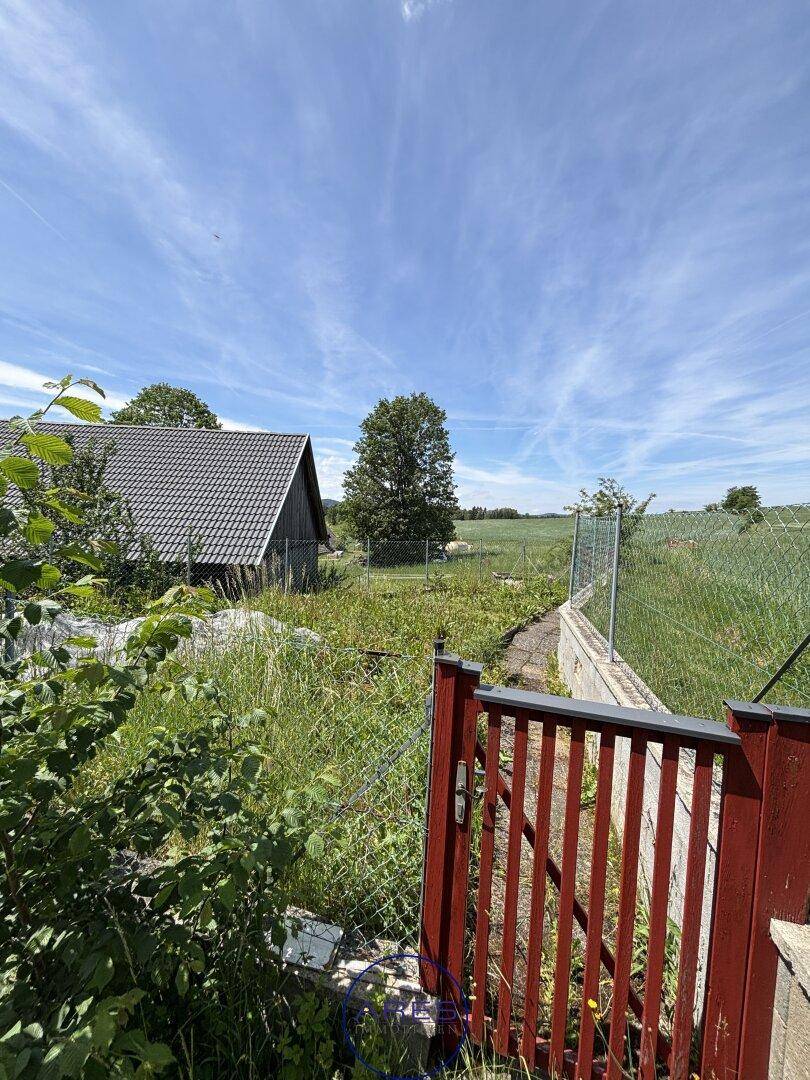 Weitläufiger Blick über grüne Felder und Wiesen mit einem roten Gartentor im Vordergrund.