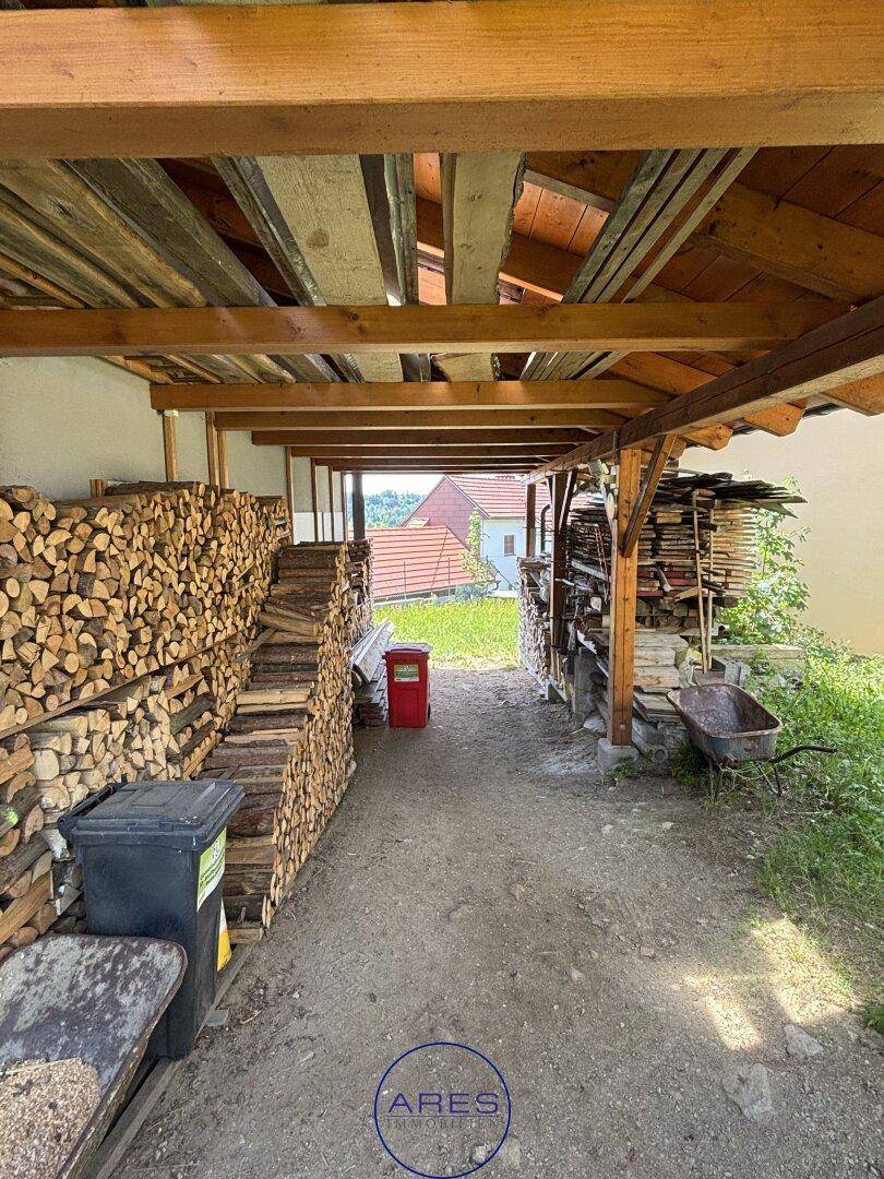 Überdachter Bereich zur Lagerung von Brennholz mit Blick auf die umliegende Landschaft.