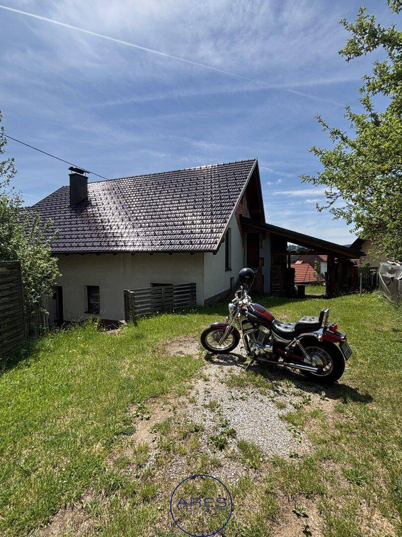 Ländliches Haus mit Satteldach und großem Gartenbereich, ein Motorrad steht im Vordergrund.