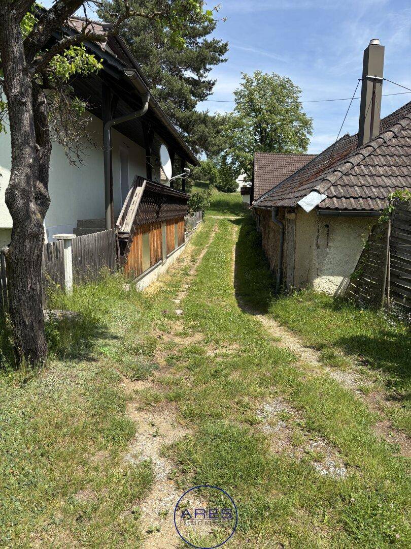 Schmaler, grasbewachsener Weg zwischen zwei Gebäuden, der in die Ferne führt.
