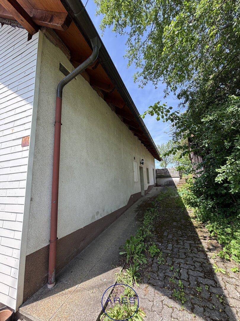 Gepflasterter Weg entlang der Hauswand, der zu einem höher gelegenen Bereich führt.