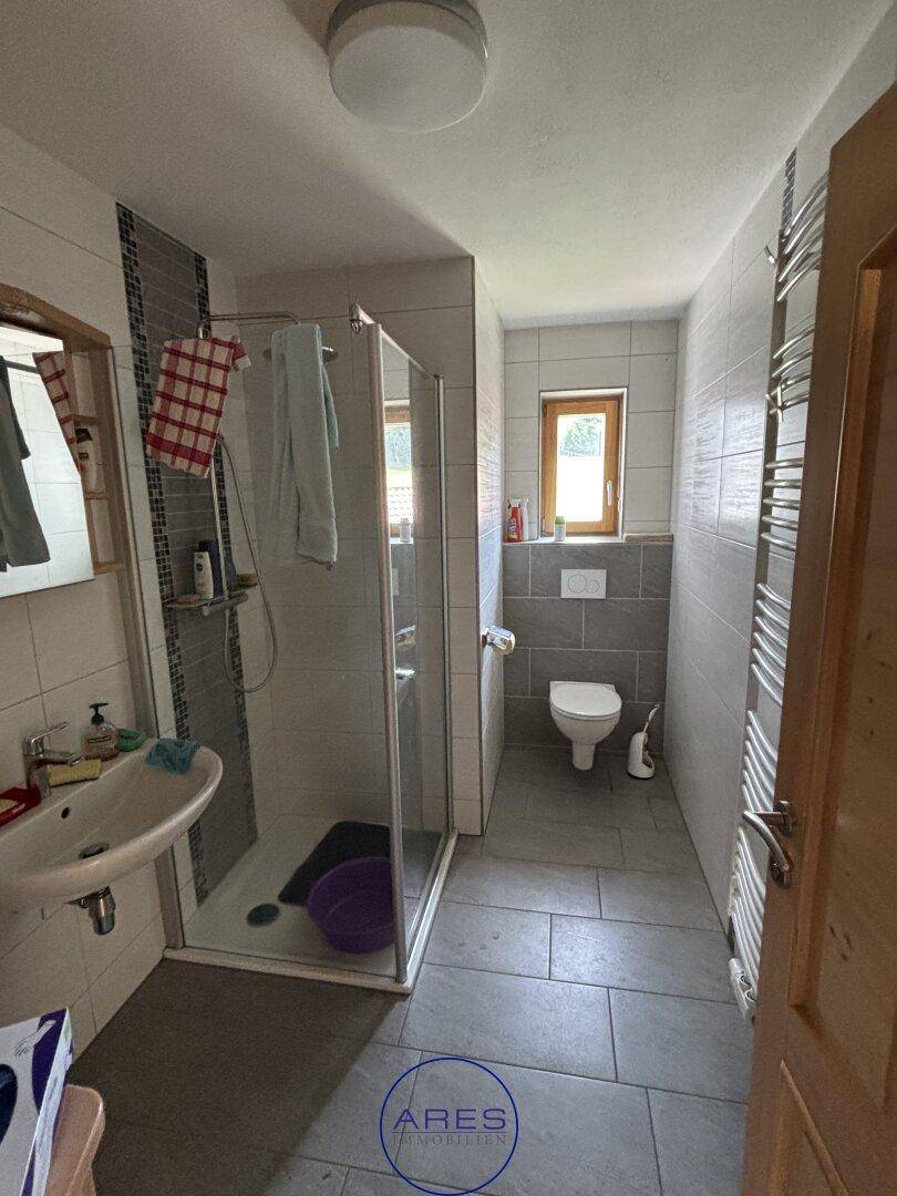 Modernes Badezimmer mit grauen Fliesen, Duschkabine und wandhängendem WC.