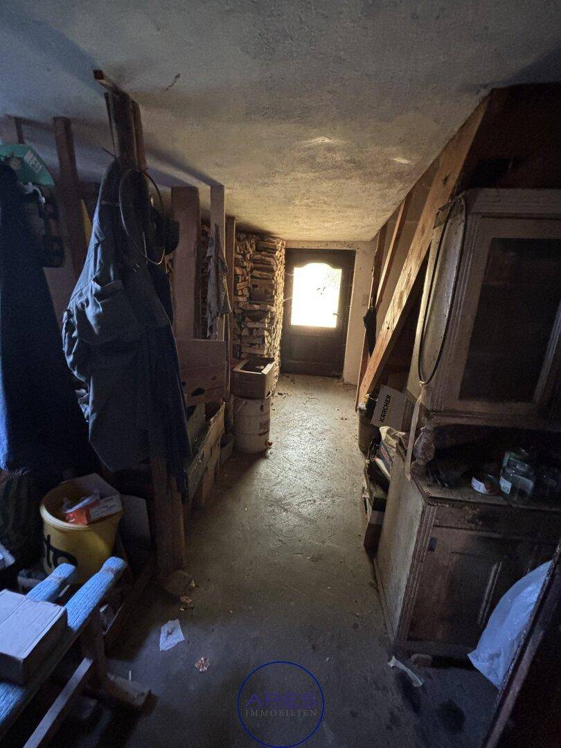 Rustikaler Flur mit Holzbalken und gestapeltem Brennholz, der zum Eingang führt.