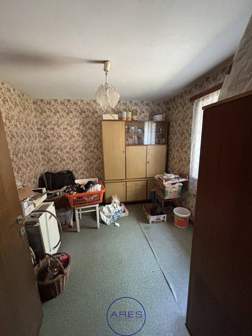 Schlafzimmer mit gemusterter Tapete, Linoleumboden und einfachen Holzmöbeln.