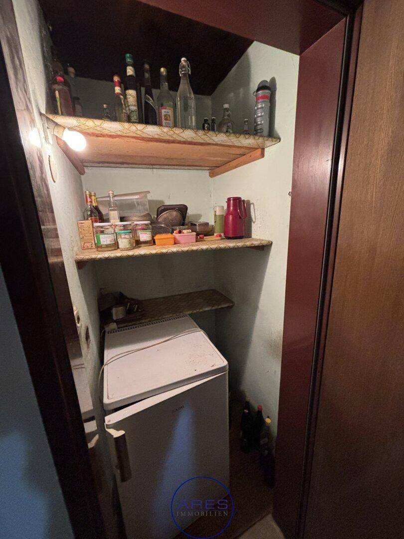 Kleine Speisekammer mit Regalen und einem Kühlschrank, ideal zur Vorratshaltung.