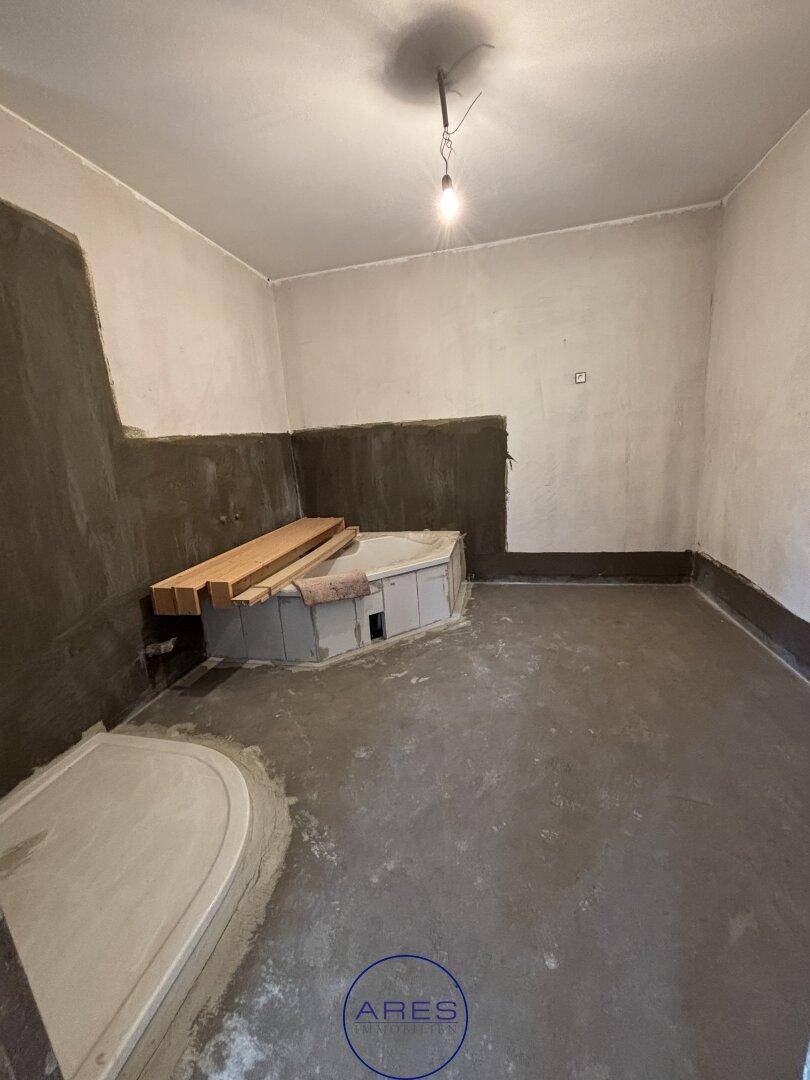 Unfertiges Badezimmer mit Eckbadewanne und vorbereiteter Holzbank, bereit für den weiteren Ausbau.