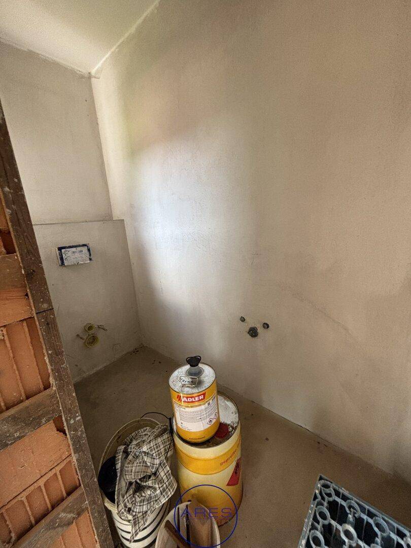 Unfertiger Raum mit sichtbaren Leitungen und Ziegelwänden, vorbereitet für die Installation einer Toilette.