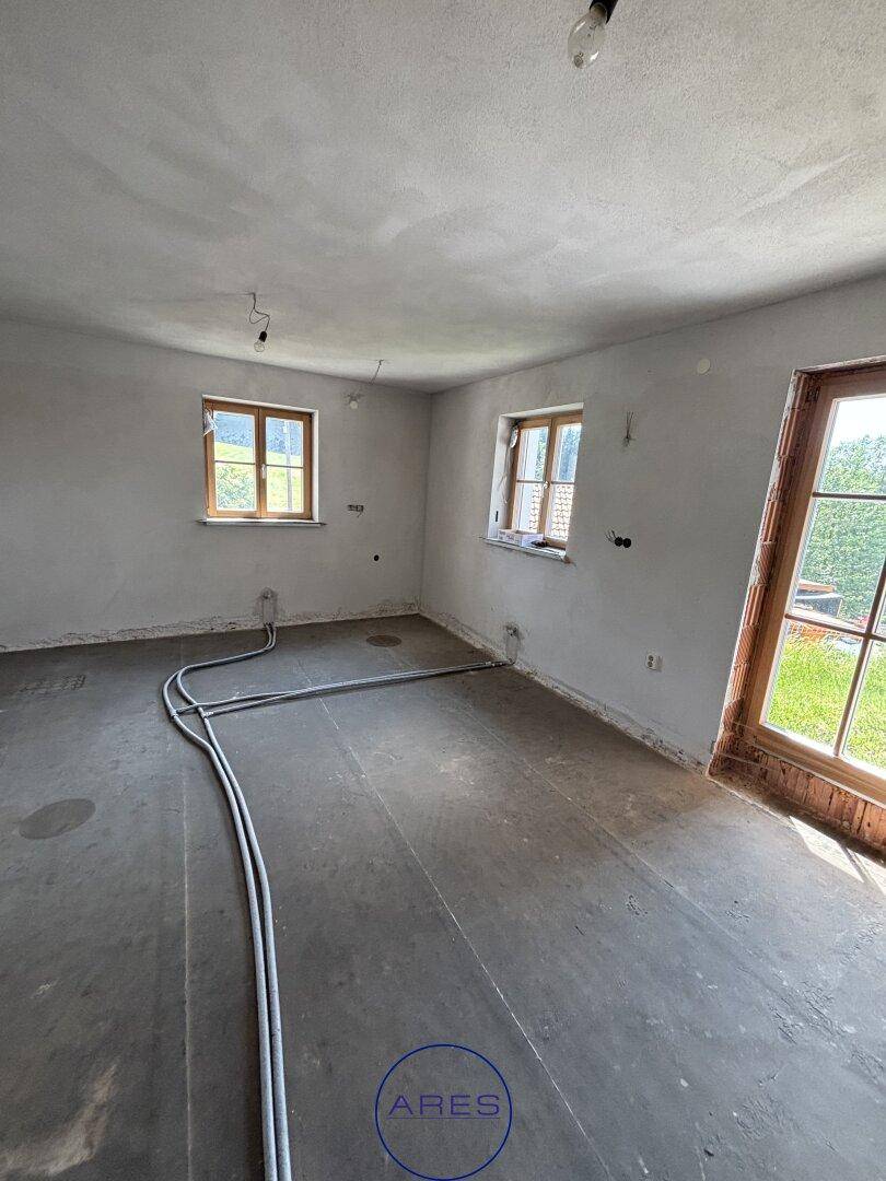 Unfertiger Raum mit Fenstern und Zugang nach draußen, vorbereitet für weitere Ausbauarbeiten.