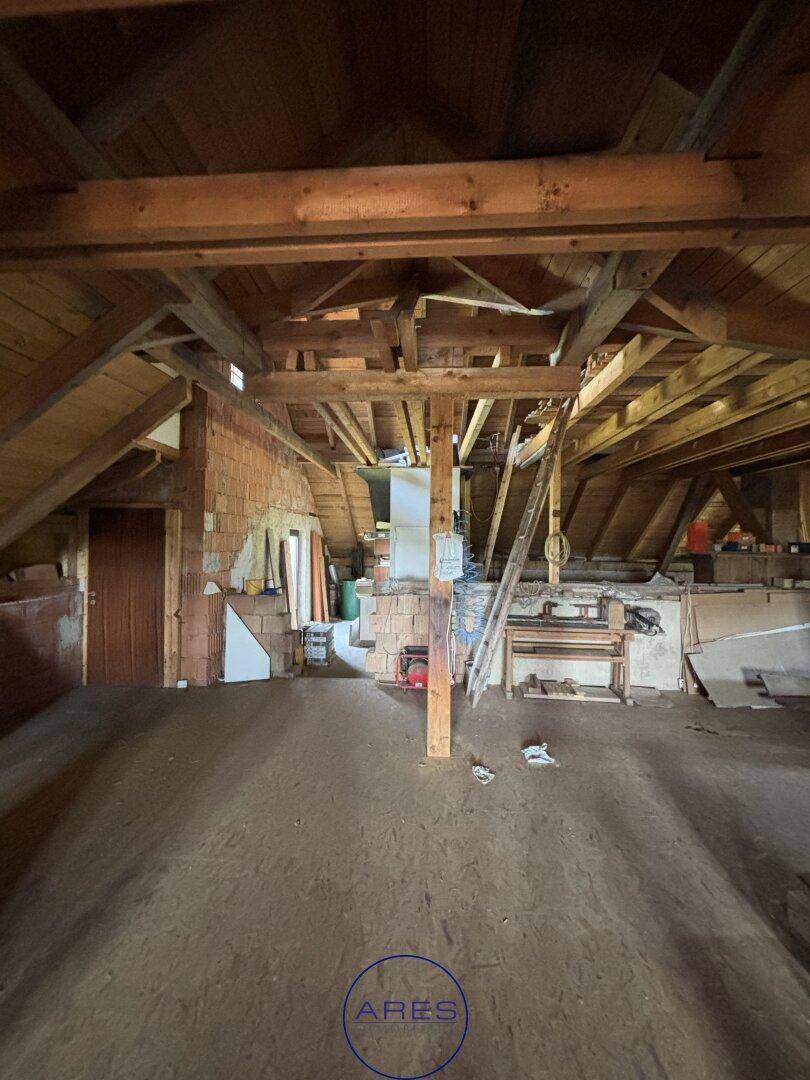 Großer Dachbodenraum mit sichtbaren Holzbalken und Ziegelwänden, bietet viel Platz für Ausbau.