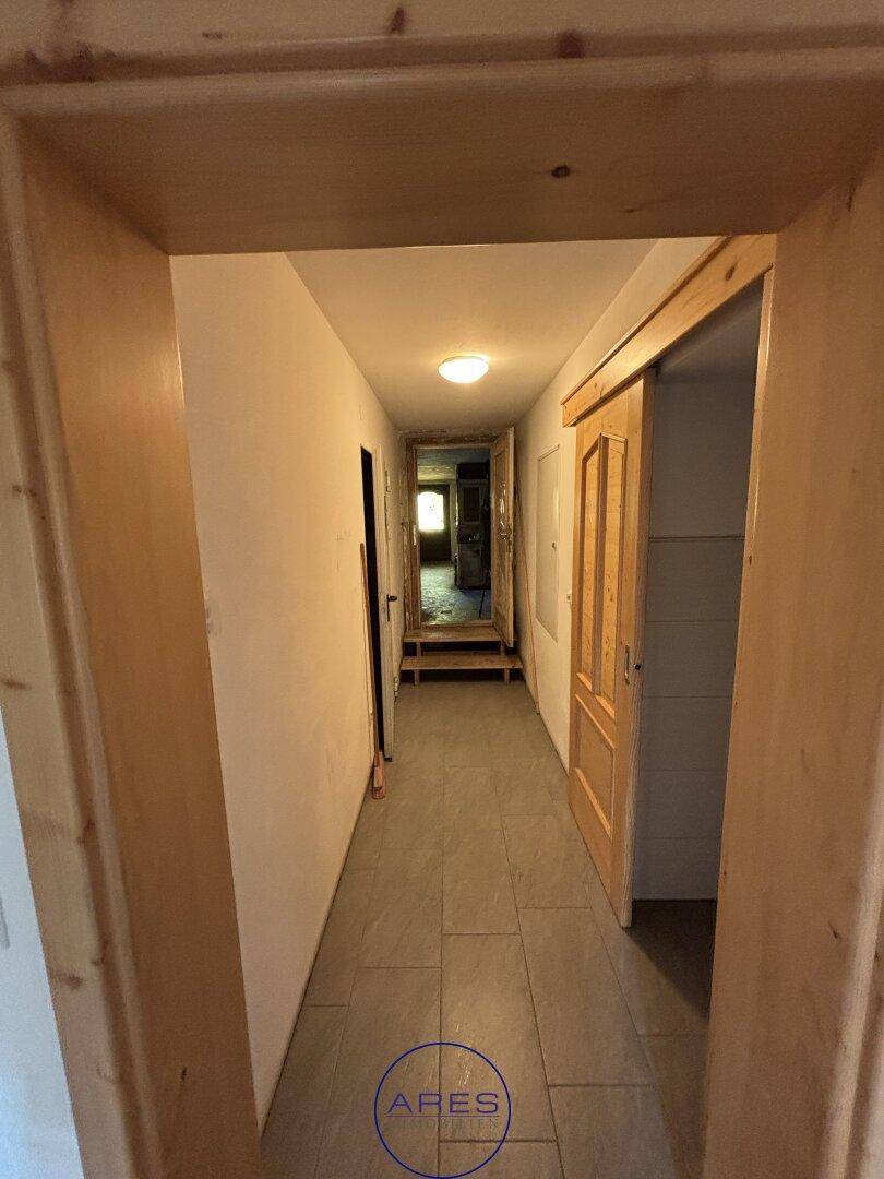 Langer Flur mit Fliesenboden und Holztüren, der zu weiteren Räumen im Haus führt.