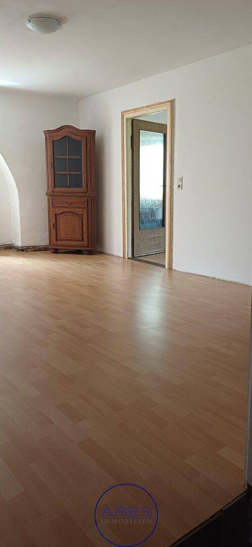 Heller Innenraum mit Laminatboden und einem klassischen Holzschrank, der zu einem weiteren Raum führt.