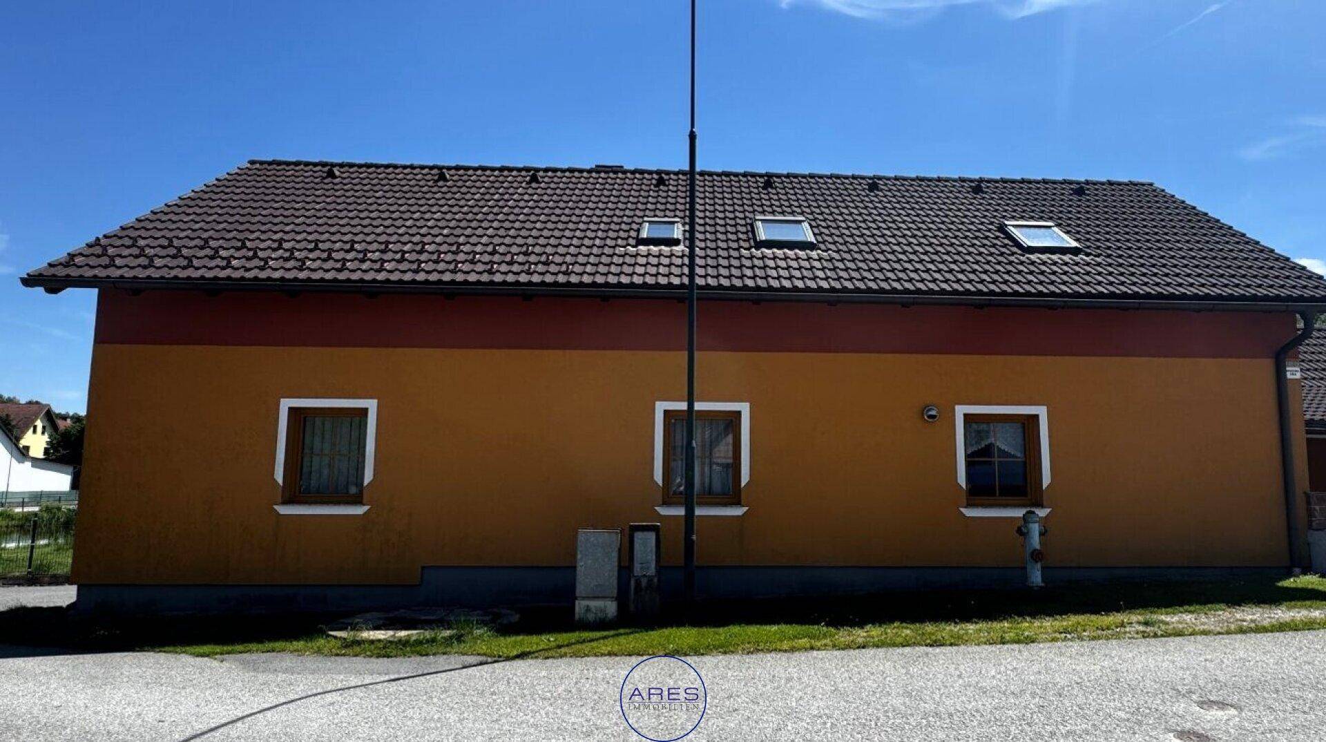 Seitenansicht des Hauses mit orangefarbener Fassade, Fenstern und einem Ziegeldach.
