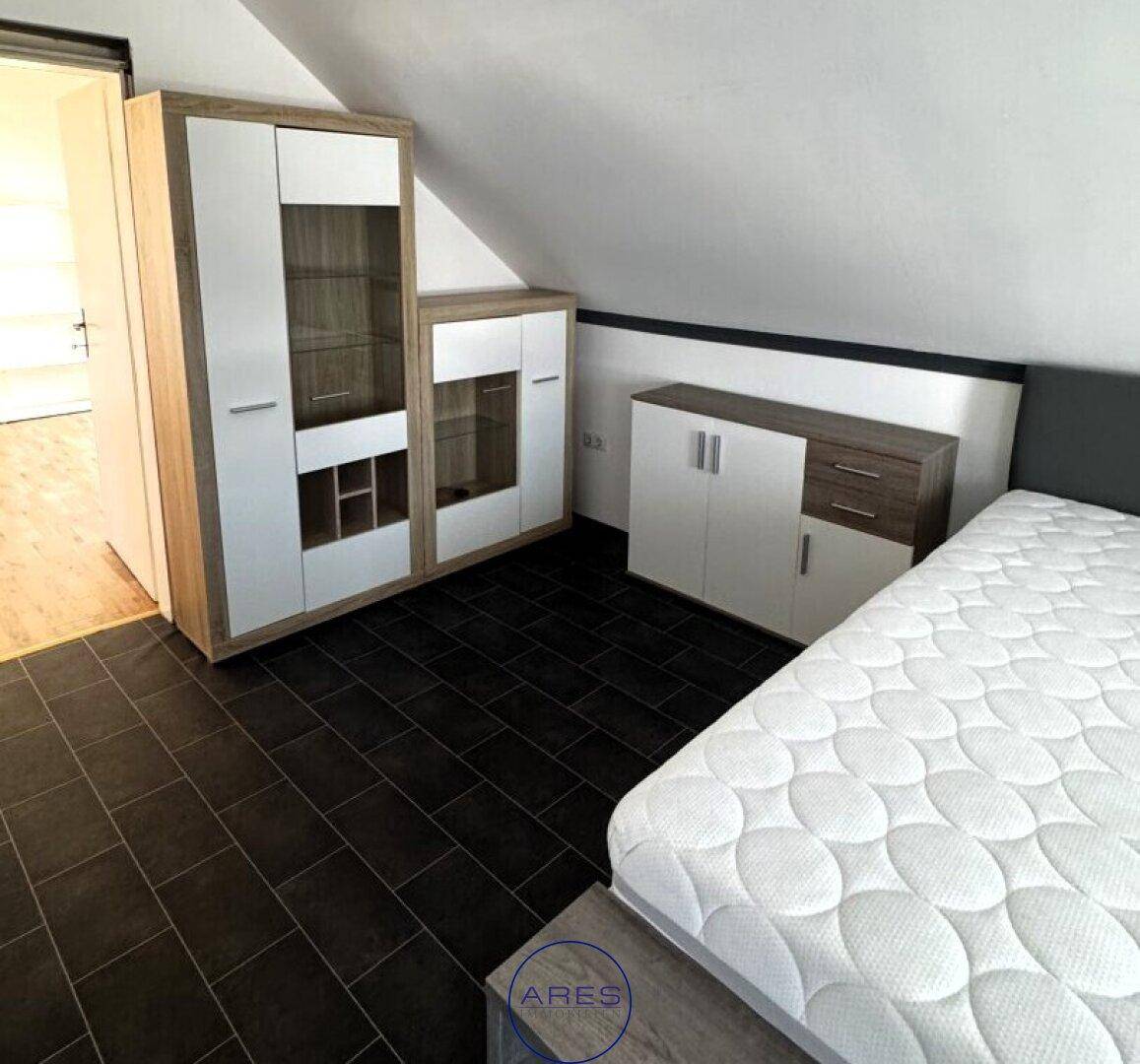 Schlafzimmer im Dachgeschoss mit dunklen Fliesen, Bett und modernen Schränken.