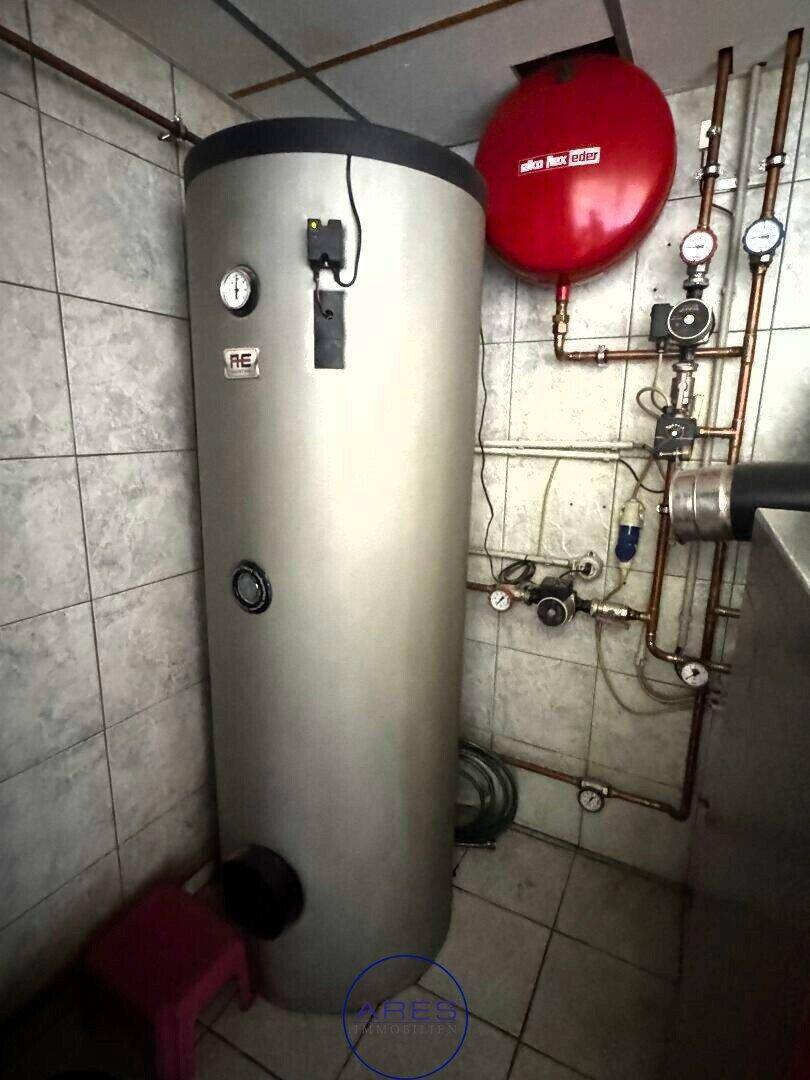 Hauswirtschaftsraum mit Warmwasserspeicher, Heizungsanlage und gefliestem Boden.