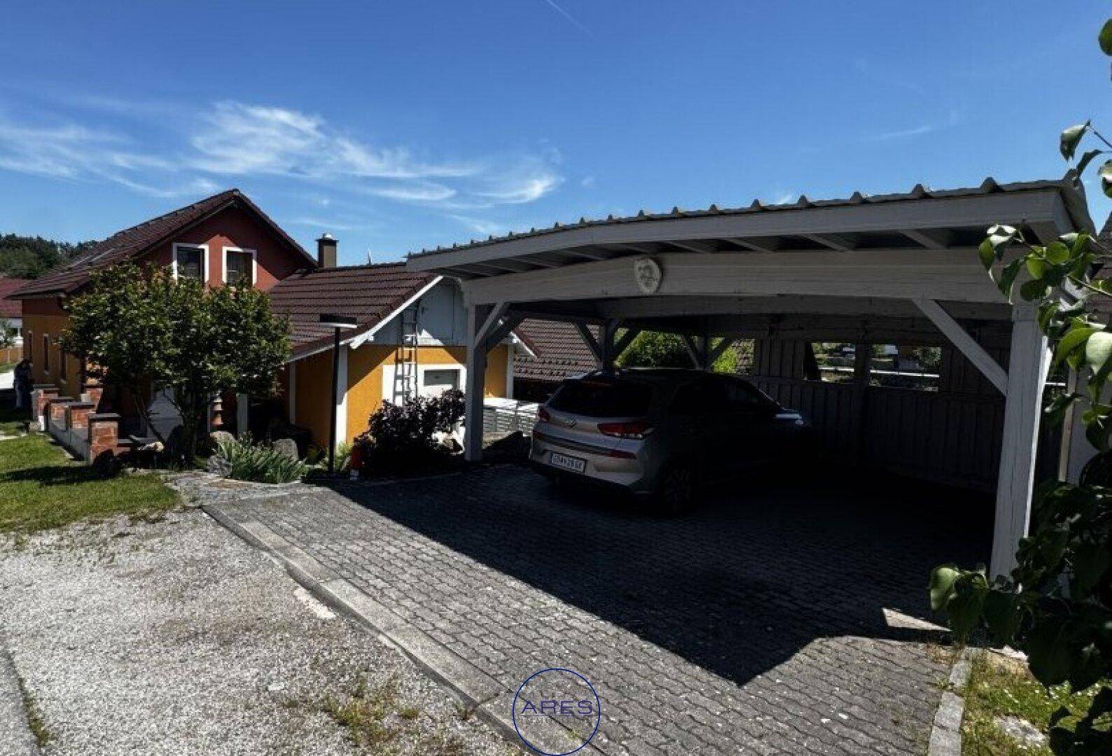 Vorderansicht des Hauses mit gepflasterter Einfahrt und einem überdachten Carport.