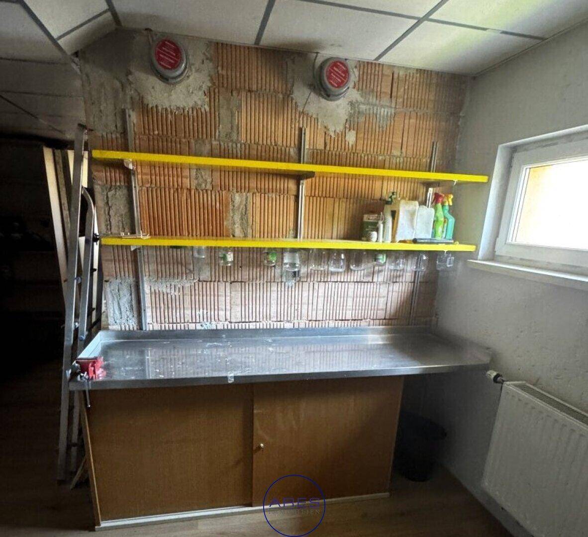Einfacher Hauswirtschaftsraum mit Werkbank, Regalen und unverputzter Ziegelwand.