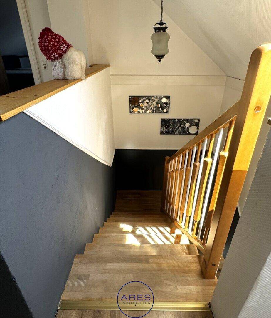 Holztreppe mit Geländer und dekorativen Bildern, die zum Dachgeschoss führt.