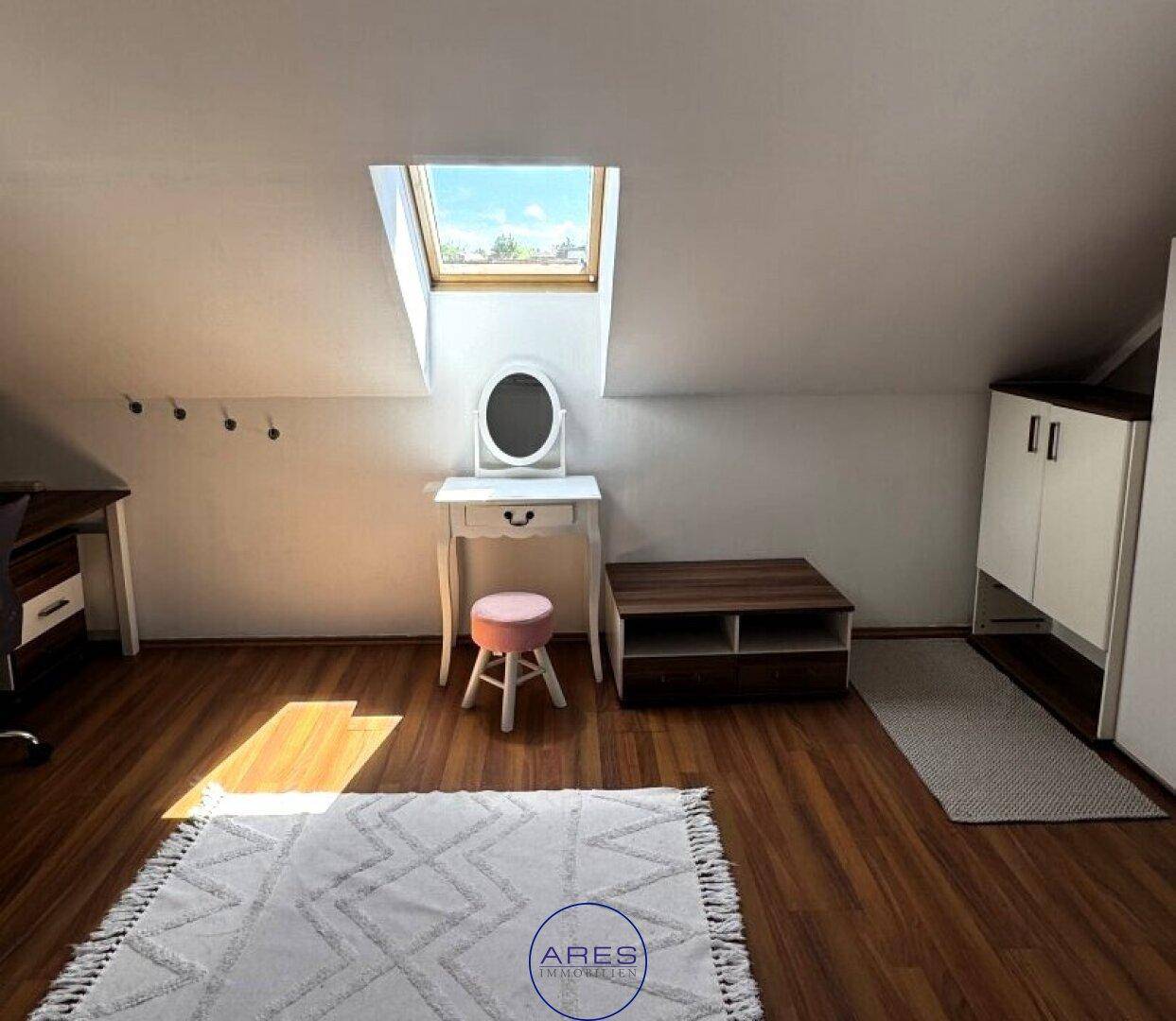 Helles Zimmer im Dachgeschoss mit Laminatboden, Schminktisch und Dachfenster.