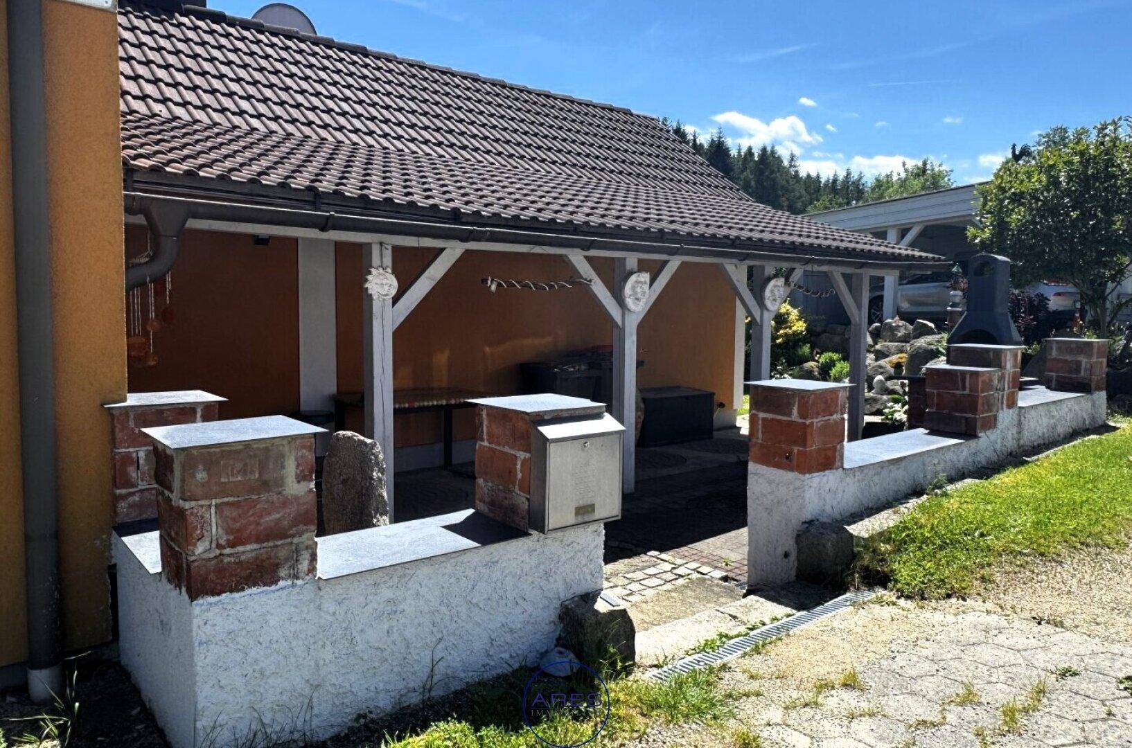 Überdachter Terrassenbereich mit gemauerten Elementen und einem Briefkasten an der Hauswand.
