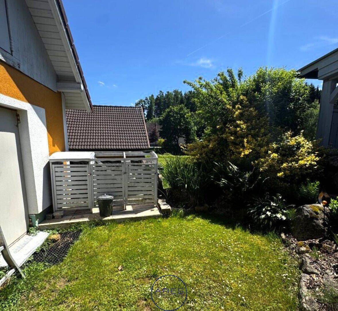 Seitlicher Gartenbereich des Hauses mit Rasenfläche und einem umzäunten Abstellbereich.