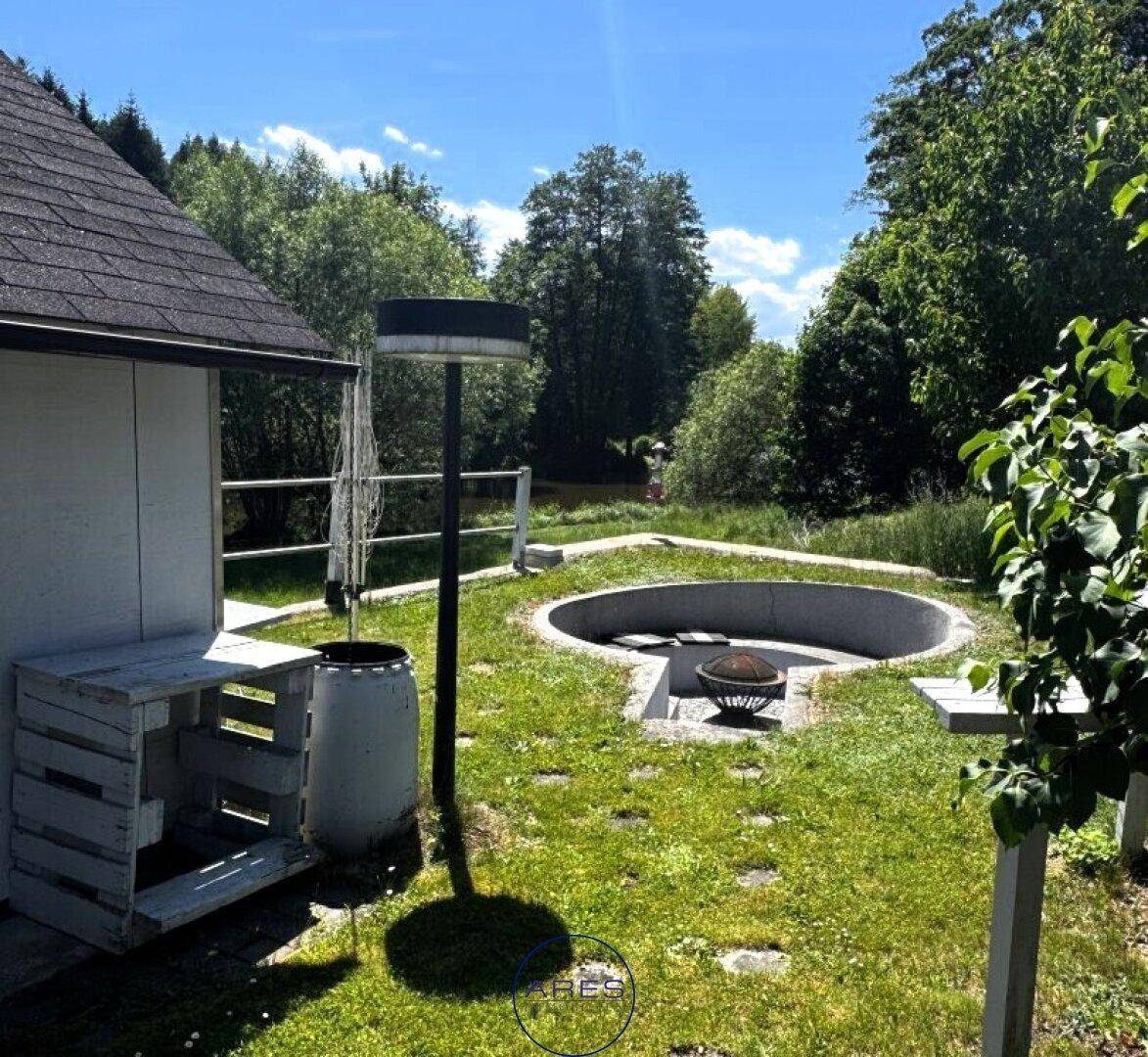 Garten mit einer runden, versenkten Feuerstelle und einem kleinen Gartenhaus im Hintergrund.