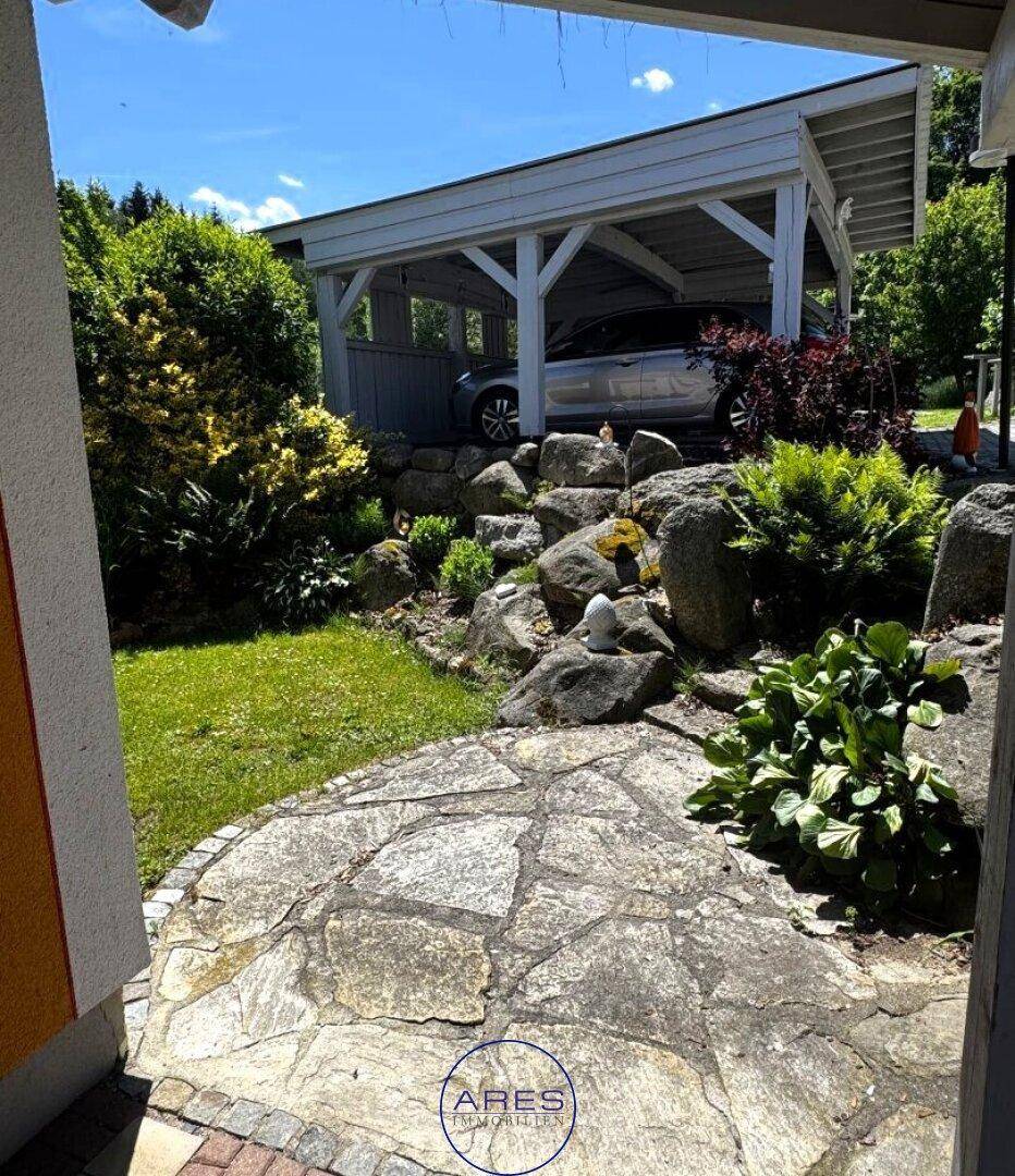 Gartenansicht mit Steingarten, Rasenfläche und einem Carport im Hintergrund.