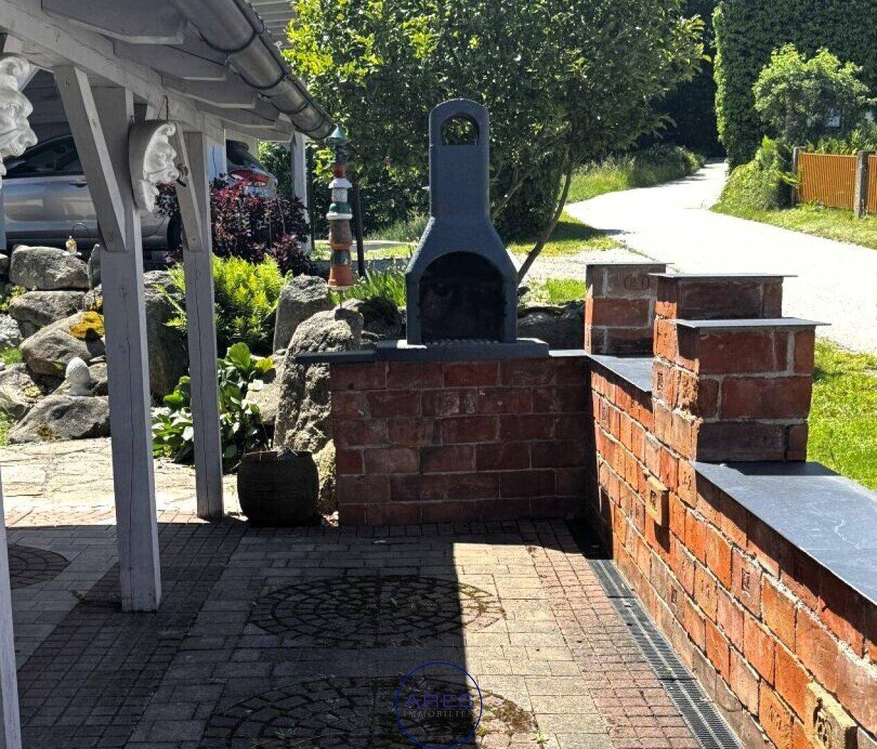 Überdachte Terrasse mit gemauertem Grill und Sitzgelegenheiten im Freien.