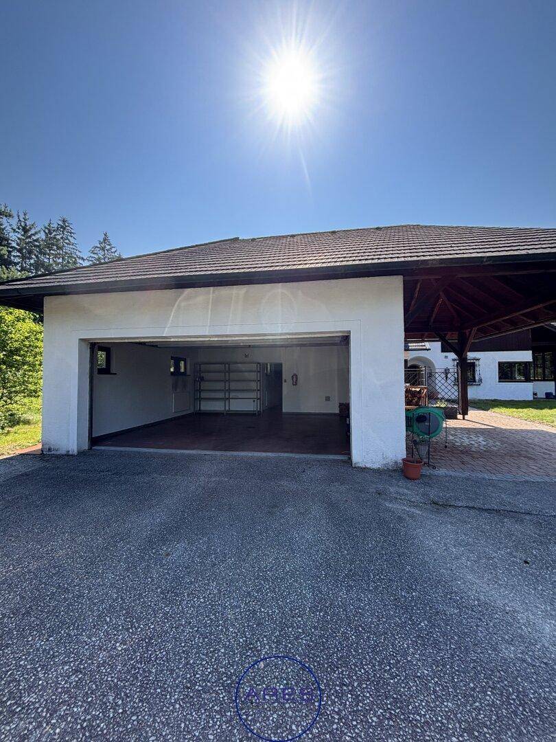 Geräumige Doppelgarage mit offenem Tor und angrenzendem Carport unter strahlendem Sonnenschein.