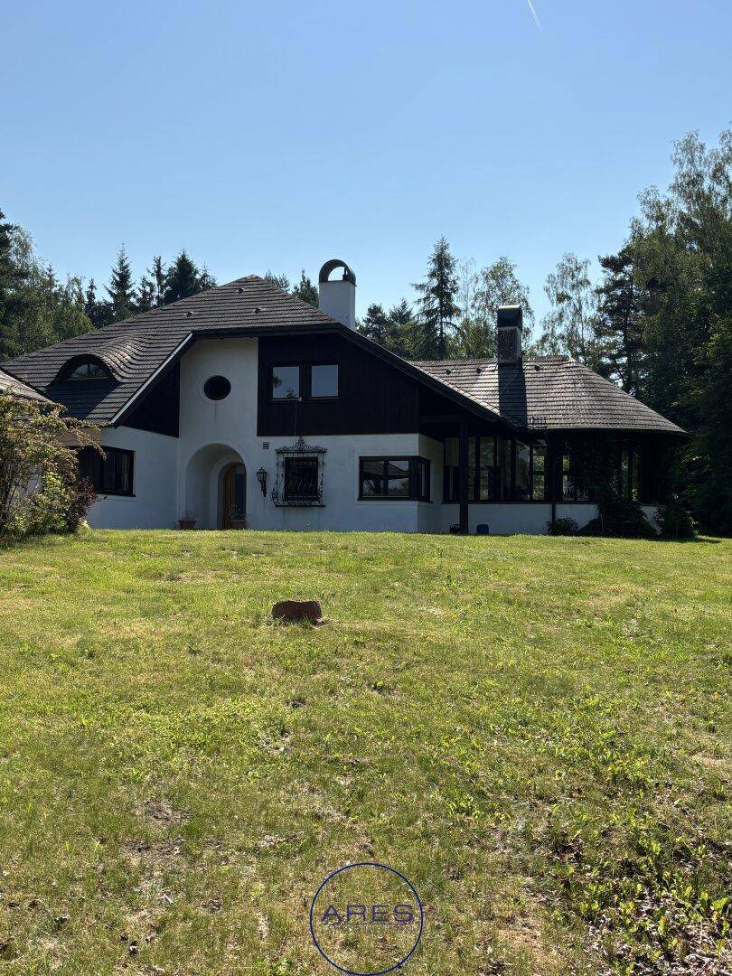 Charmantes Landhaus mit weißer Fassade und dunklem Dach, umgeben von einer grünen Rasenfläche.