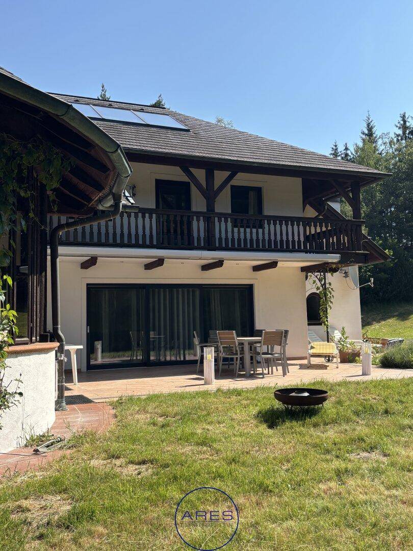 Sonniger Terrassenbereich mit Gartenmöbeln und Zugang zum Garten, darüber ein Balkon mit Holzgeländer.