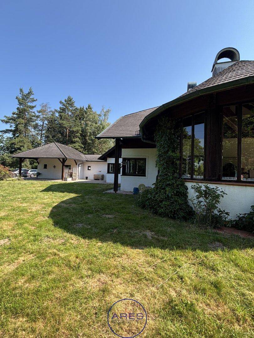 Seitliche Ansicht des Landhauses mit großen Fenstern und üppiger Begrünung an der Fassade.