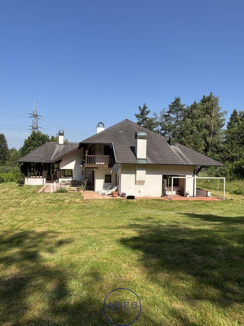 Großzügiger Gartenbereich mit weitläufiger Rasenfläche und Blick auf das Landhaus unter blauem Himmel.
