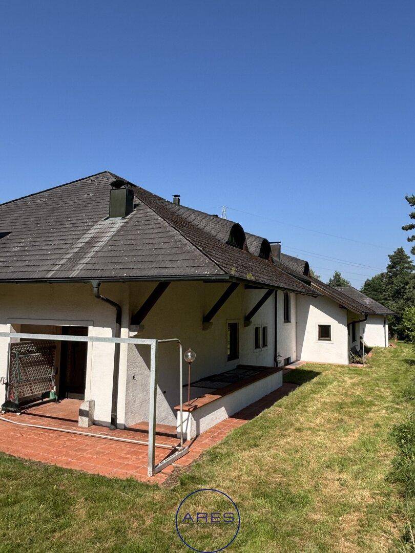 Seitliche Ansicht des Hauses mit einer gepflasterten Terrasse und Zugang zum weitläufigen Gartenbereich.