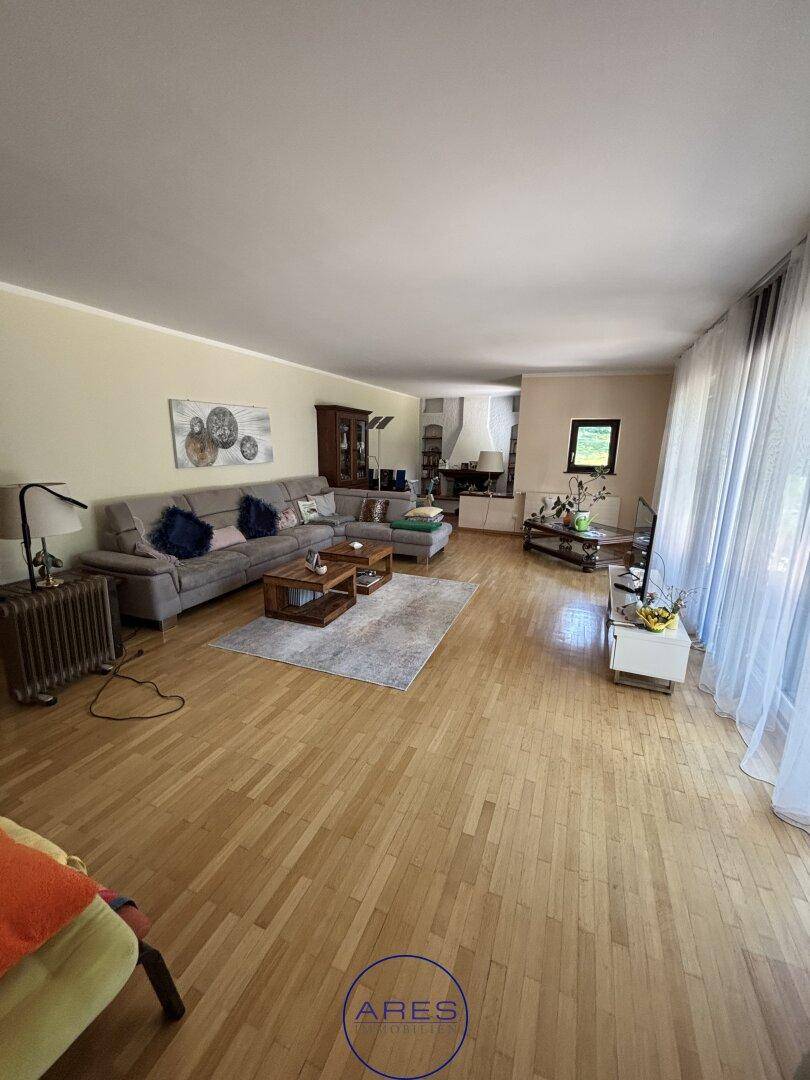Helles Wohnzimmer mit großem Sofa, Holzboden und bodentiefen Fenstern mit Zugang zur Terrasse.