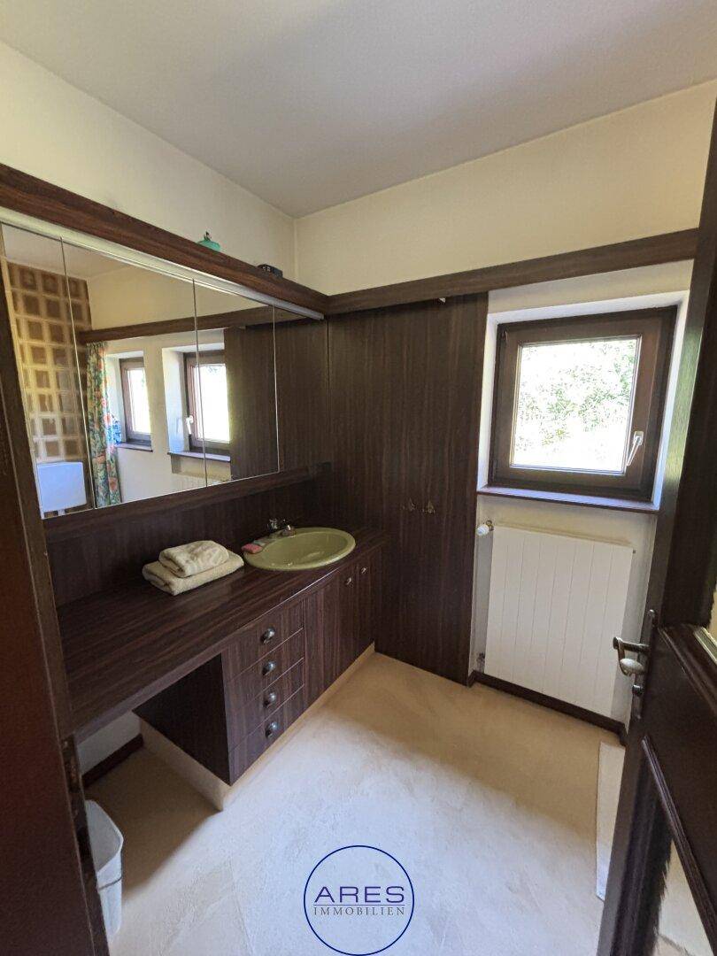 Badezimmer mit Holzmöbeln, integriertem Waschbecken und großem Spiegelschrank.