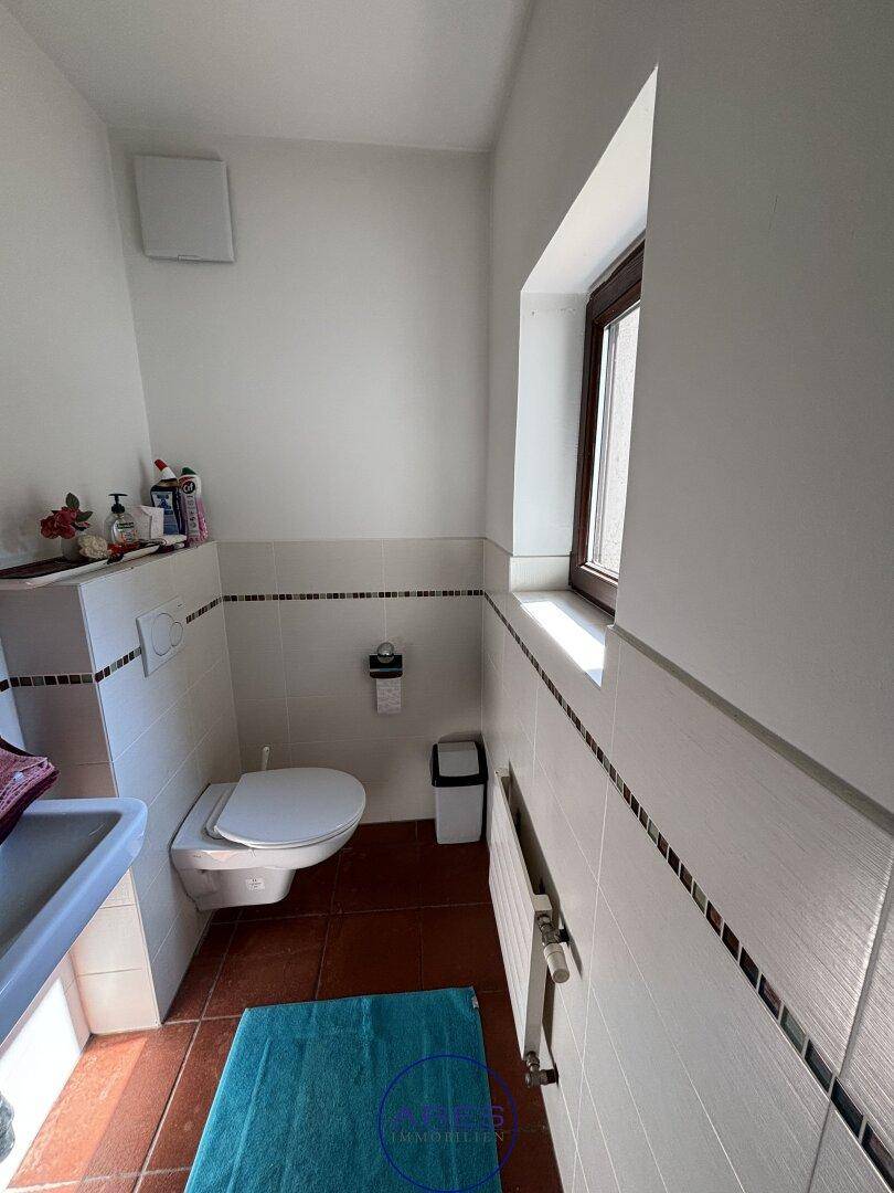 Kleines Gäste-WC mit weißen Fliesen, Toilette und Fenster.