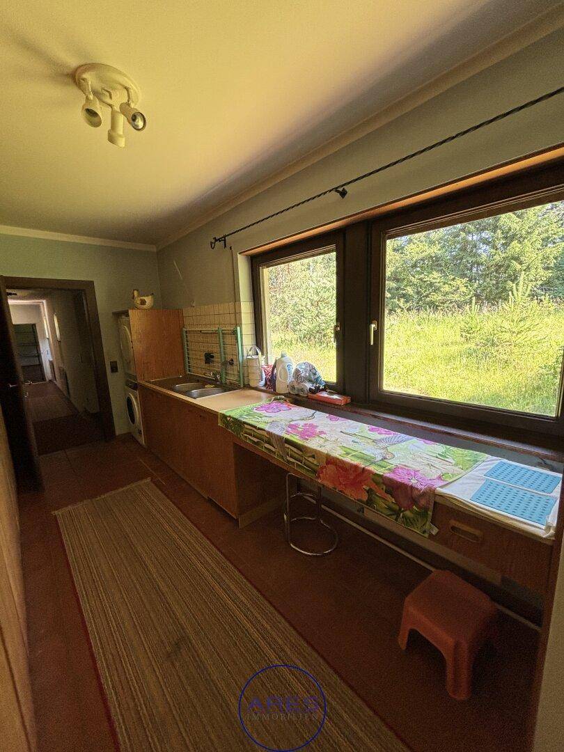 Einfache Küche mit Arbeitsplatte, Spüle und großem Fenster mit Blick ins Grüne.