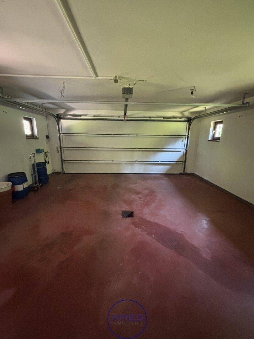 Geräumige Garage mit rotem Betonboden und großem Garagentor.