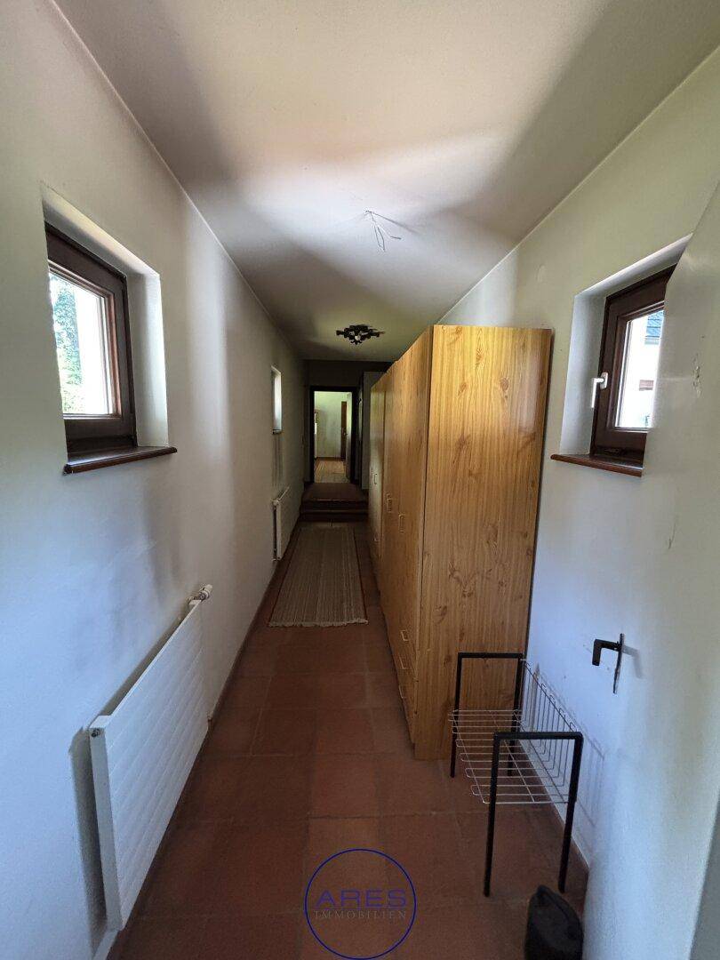 Langer Flur mit Terrakottafliesen, Holzschrank und Fenstern.