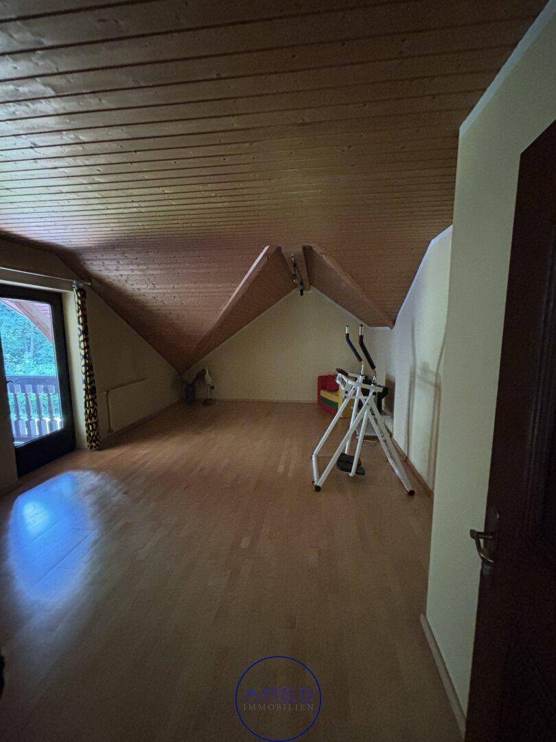 Dachgeschosszimmer mit Holzdecke, Holzboden und Zugang zum Balkon.